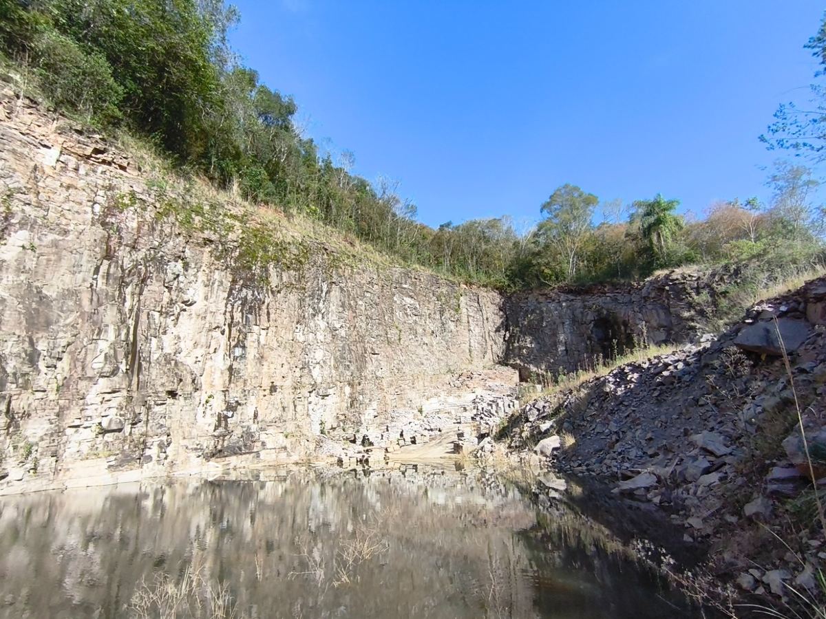 Parede de basalto de uma cava refletida no espelho d'água, com mata nativa no topo